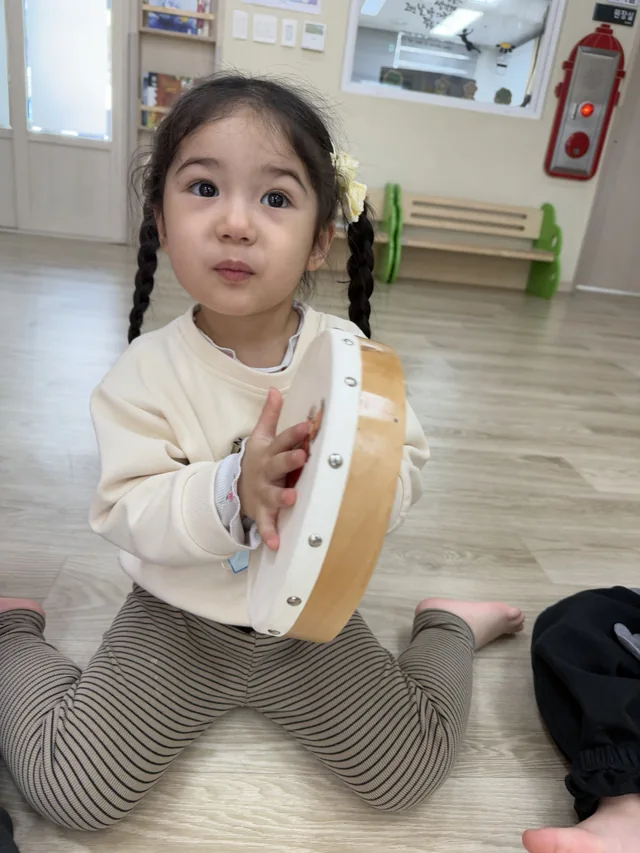 바닥에 앉아 탬버린을 들고 놀이에 집중하는 일린